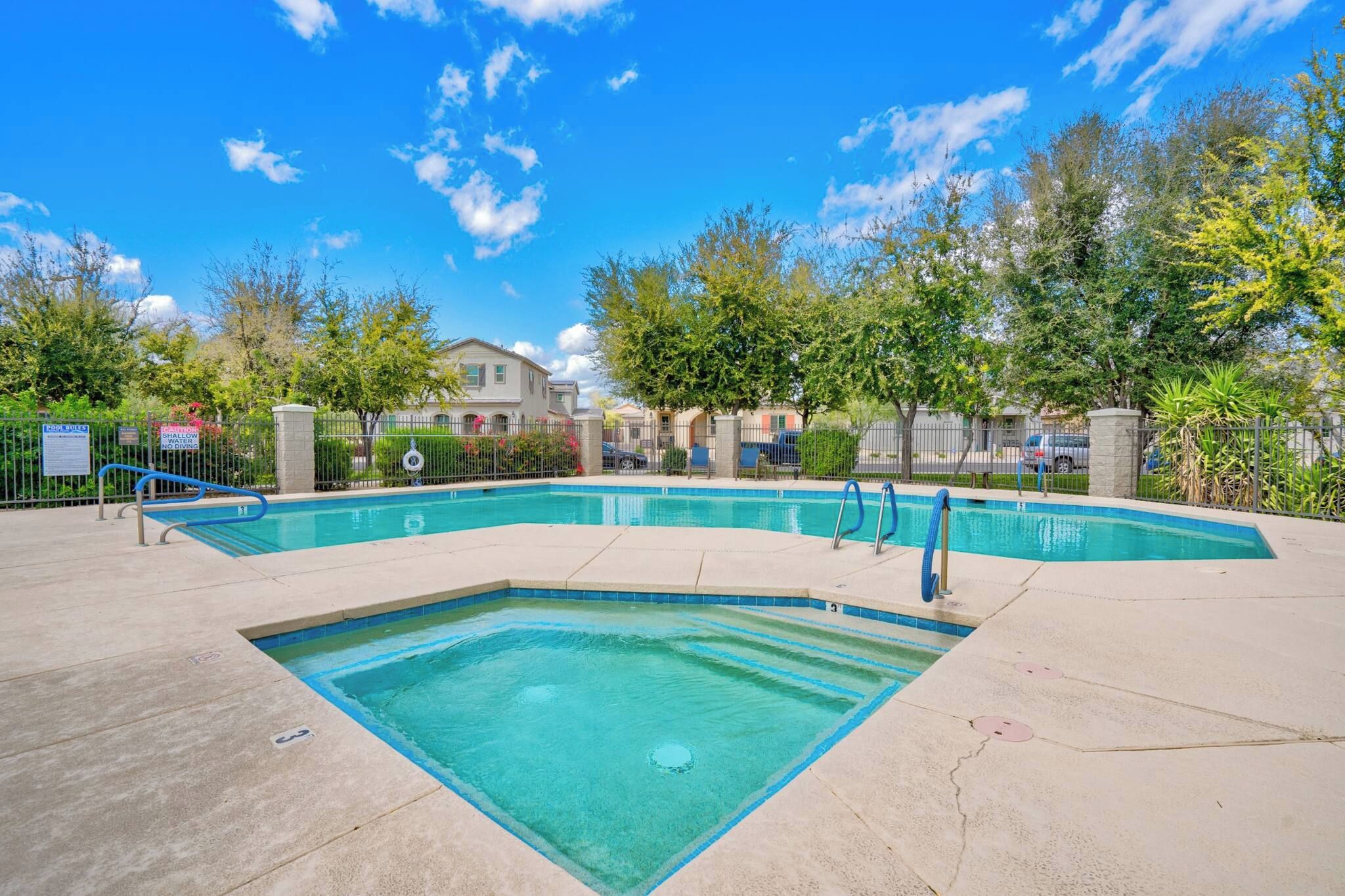 A rectangular swimming pool with a diving board, surrounded by a fence and trees.