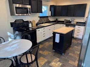 A modern kitchen with dark cabinetry, a built-in microwave, a stove, and a small island with a sink. - Cozy 1-bedroom bungalow in historic North End of Boise with AC and sauna (Boise)
