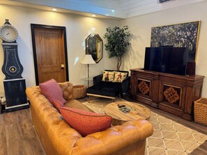 Un salon comprenant un canapé, une table basse, un téléviseur, une horloge et un miroir.