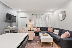 A modern living room with a sofa, coffee table, and a flat-screen TV mounted on the wall. - HiTide Condo | Walk to Campus | Prime Gameday Unit (Tuscaloosa)