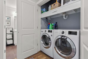 Una sala de bugaderia amb dues màquines de rentar de càrrega frontal, una estant amb productes de neteja i una prestatgeria amb tovalloles pliegades.