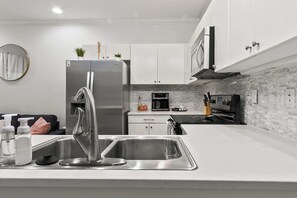 A modern kitchen with stainless steel appliances, a double sink, and a coffee maker. - HiTide Condo | Walk to Campus | Prime Gameday Unit (Tuscaloosa)