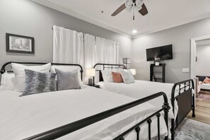 Een hotelkamer met twee bedden, een plafondventilator, een flatscreen televisie en een ingelijste foto aan de muur.