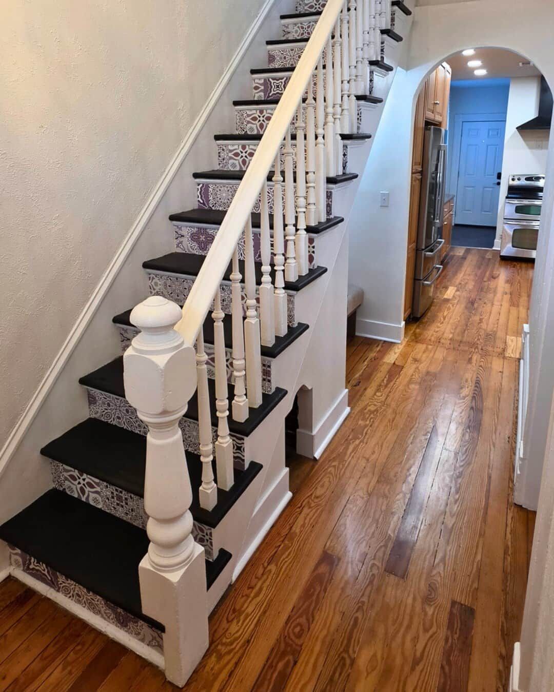 A staircase with patterned steps and white balusters leading to a kitchen area with wooden flooring.