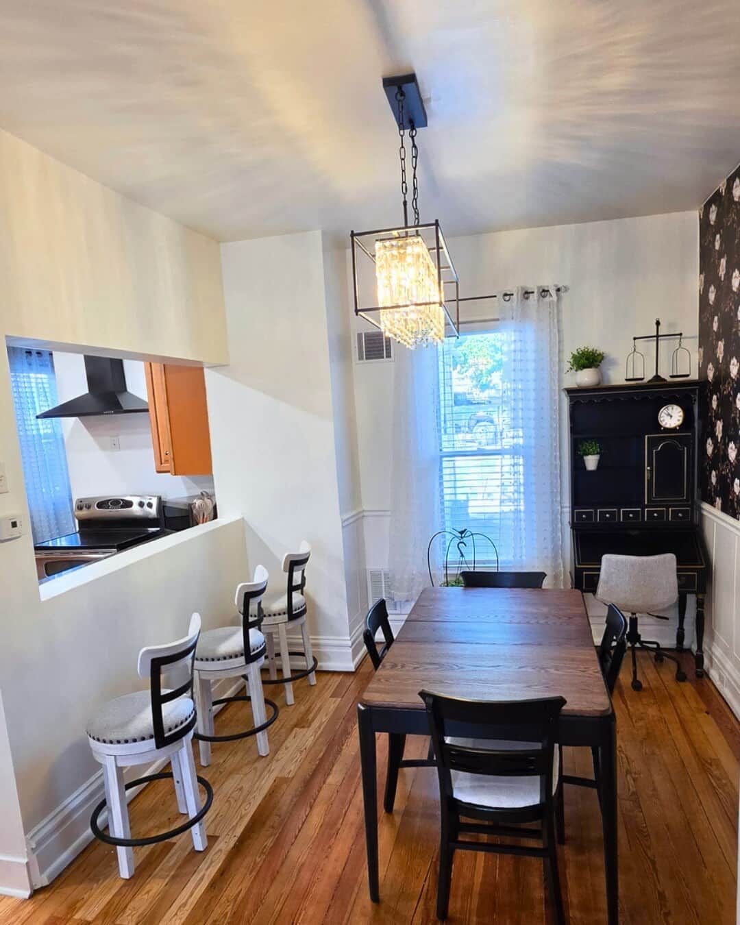 A dining area with a wooden table and chairs, a kitchen with a stove and cabinets, and a chandelier.