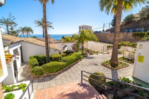 A courtyard with a paved walkway, palm trees, and a view of the sea. - House in Nerja Near El Playazo Beach (Nerja)