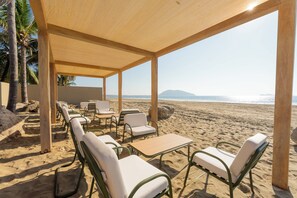A beachside seating area with tables and chairs under a wooden canopy, overlooking the beach and ocean. - Oceanfront Sunsets and Private Pool in Playa Blanca (Playa Blanca)