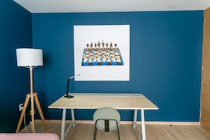 Um quarto com parede azul, um quadro branco com um tabuleiro de xadrez, uma escrivaninha, uma cadeira e um abajur.
