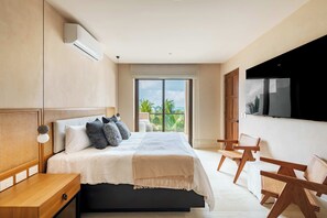Ein modernes Schlafzimmer mit einem großen Bett, einem Fernseher und einem Balkon mit Blick auf Palmen.