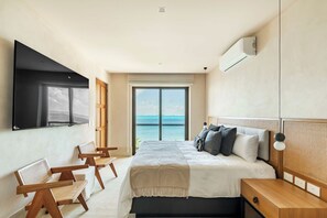 A modern bedroom with a large bed, a TV mounted on the wall, and a view of the ocean through a large window. - Artila Isla Mujeres: Exclusive Oceanview Stay with Pool & Beach Access (Isla Mujeres)
