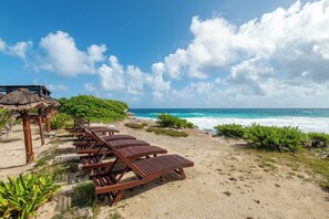 A beach with wooden lounge chairs and a thatched-roof structure.