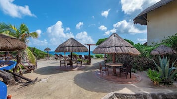 Un complexe hôtelier en bord de mer, doté de parasols en chaume, de chaises longues et offrant une vue sur l’océan.