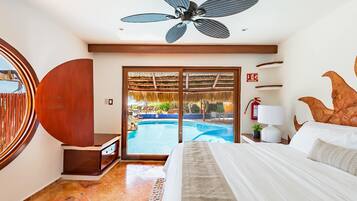 Habitación de hotel con cama, ventilador de techo, vista a una piscina al aire libre y un extintor en la pared.