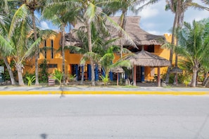 A yellow building with thatched roofs, surrounded by palm trees. - Bella Mar: Ocean Front w/ Pool Views (Isla Mujeres)