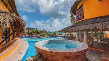 Zona de piscina en un resort con un jacuzzi, estructuras de techo de paja y mobiliario de exterior.