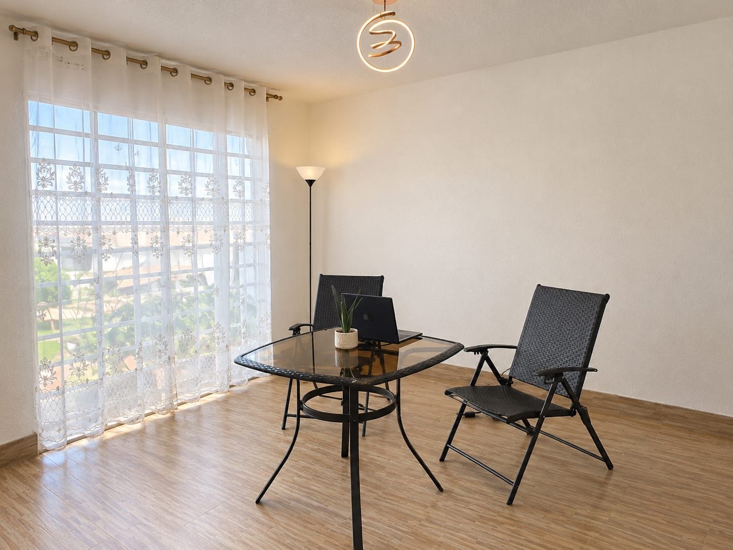 Una habitación con una mesa de vidrio, dos sillas, una computadora portátil y una lámpara.