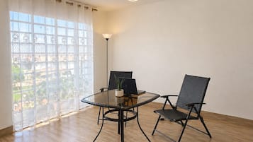 A room with a glass table, two chairs, a laptop, and a lamp.
