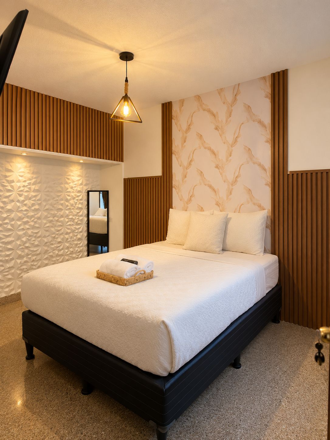 Une chambre d’hôtel moderne avec un grand lit, une tête de lit en bois, un mur à motifs et un luminaire suspendu.
