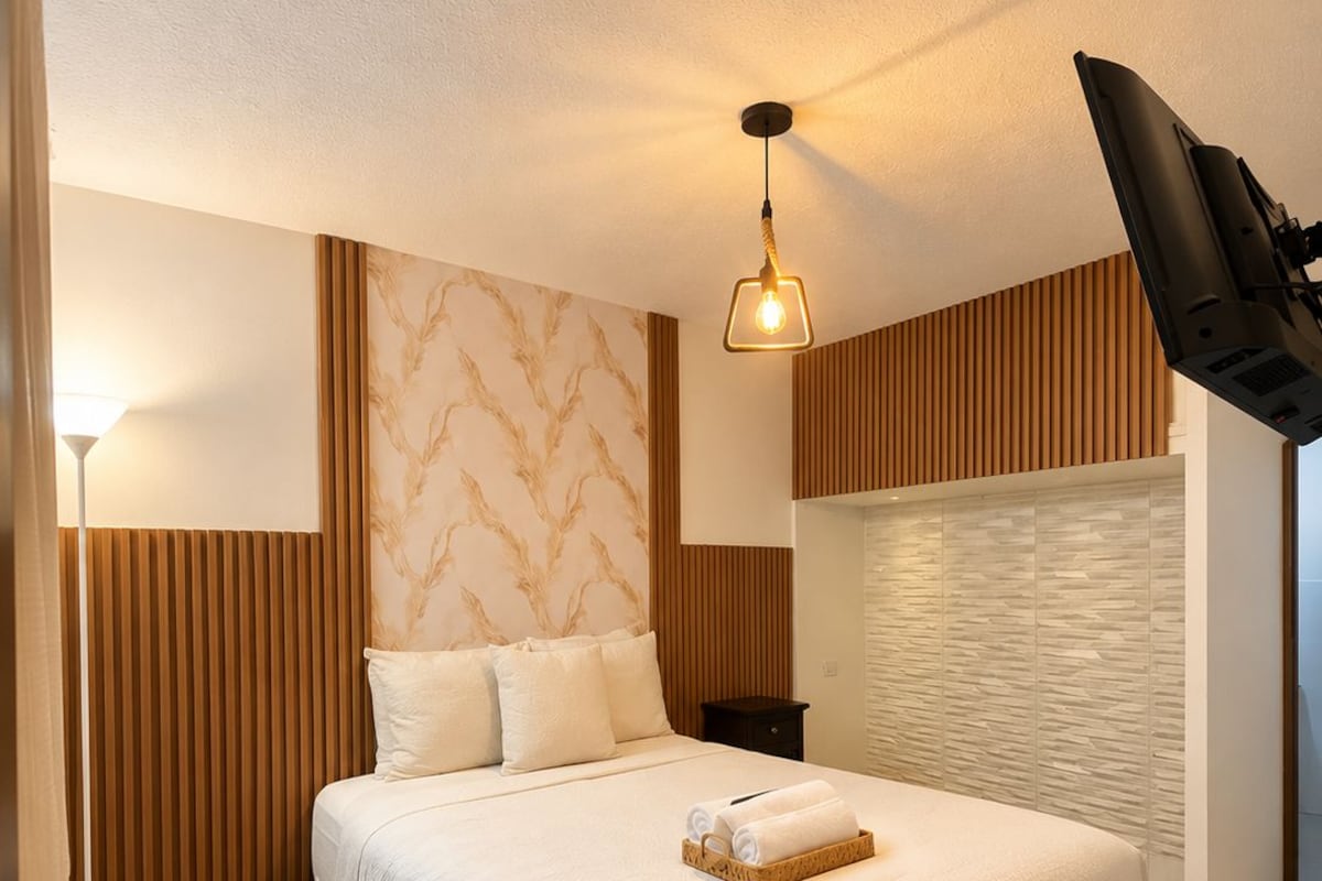 A hotel room with a bed, a nightstand, a lamp, and a television.