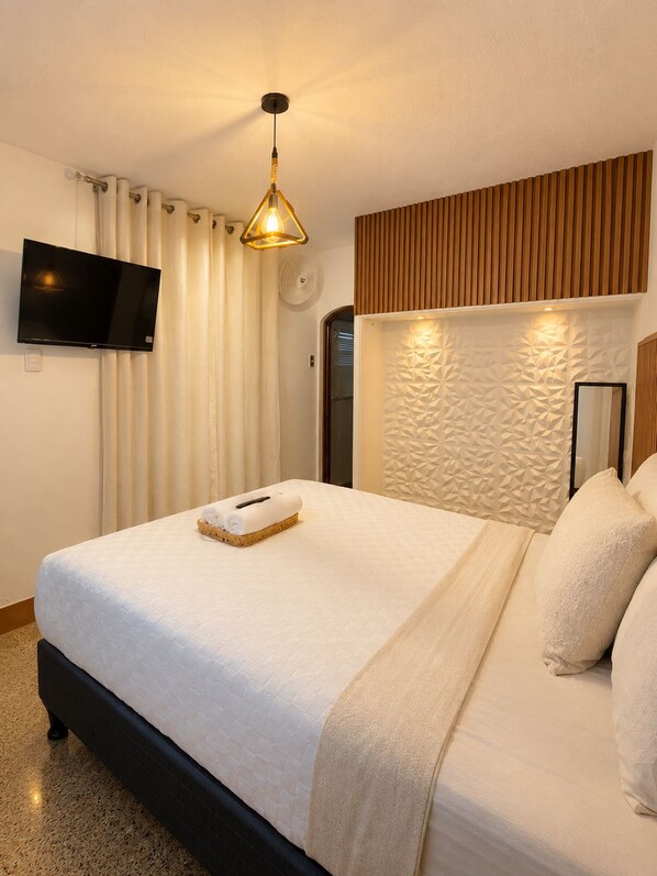 A hotel room with a bed, a flat-screen TV, a wall-mounted light fixture, and a textured wall panel.