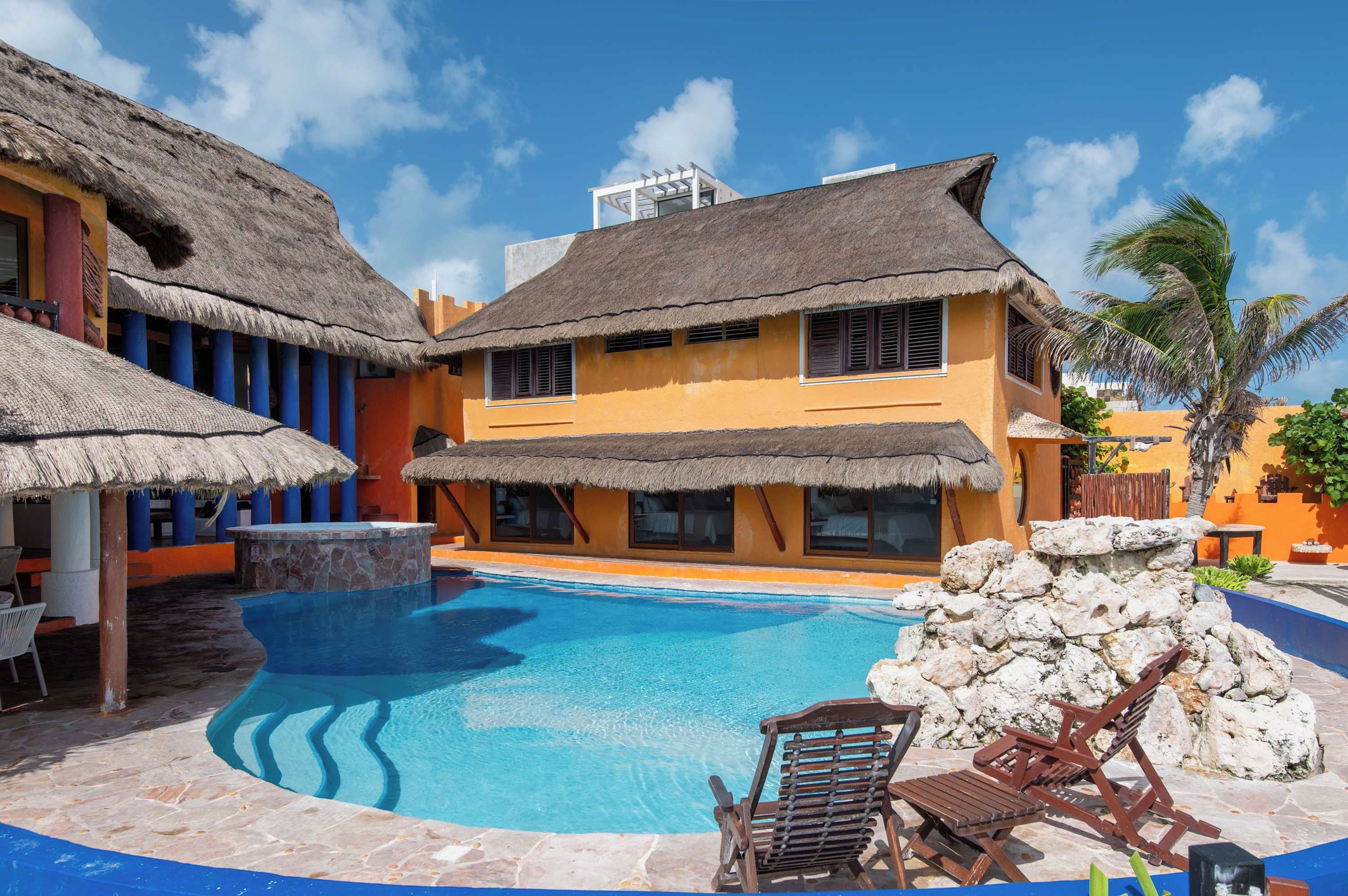 Um resort com piscina, edifícios com telhados de palha e uma parede de pedra.