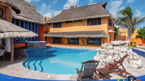 Um resort com piscina, edifícios com telhados de palha e uma parede de pedra.