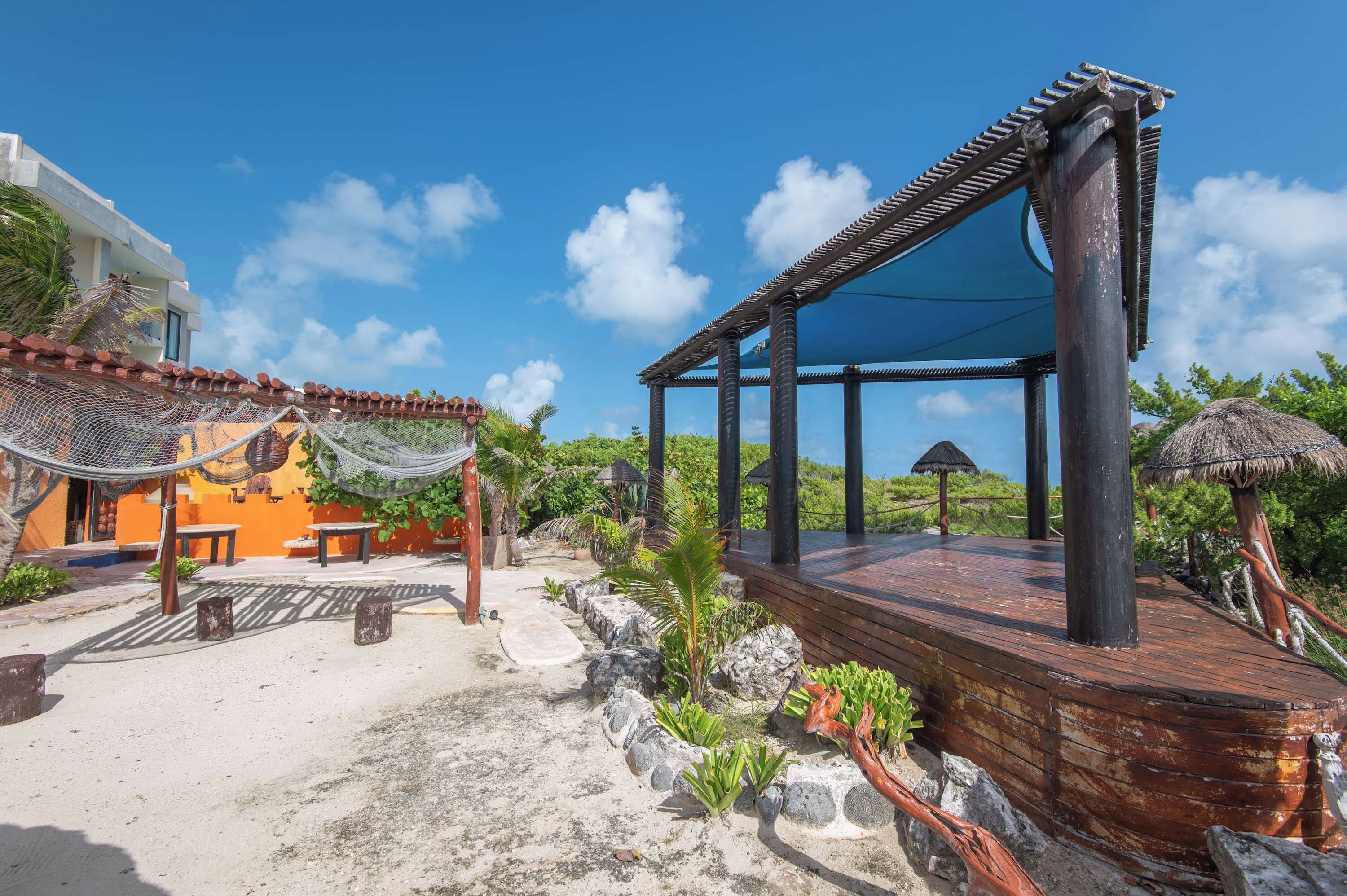 A beachside resort with a wooden deck, outdoor seating, and a thatched-roof structure.