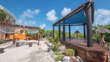A beachside resort with a wooden deck, outdoor seating, and a thatched-roof structure.