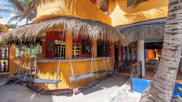 Un edificio con techo de paja, una zona de bar con columpios y una palmera.