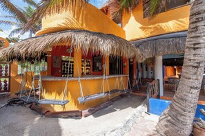 A building with a thatched roof, a bar area with swings, and a palm tree. - Bella Mar: Ocean Front w/ Pool Views (Isla Mujeres)