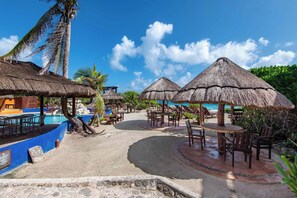 A beachside resort with thatched umbrellas, lounge chairs, and a pool area. - Bella Mar: Ocean Front w/ Pool Views (Isla Mujeres)