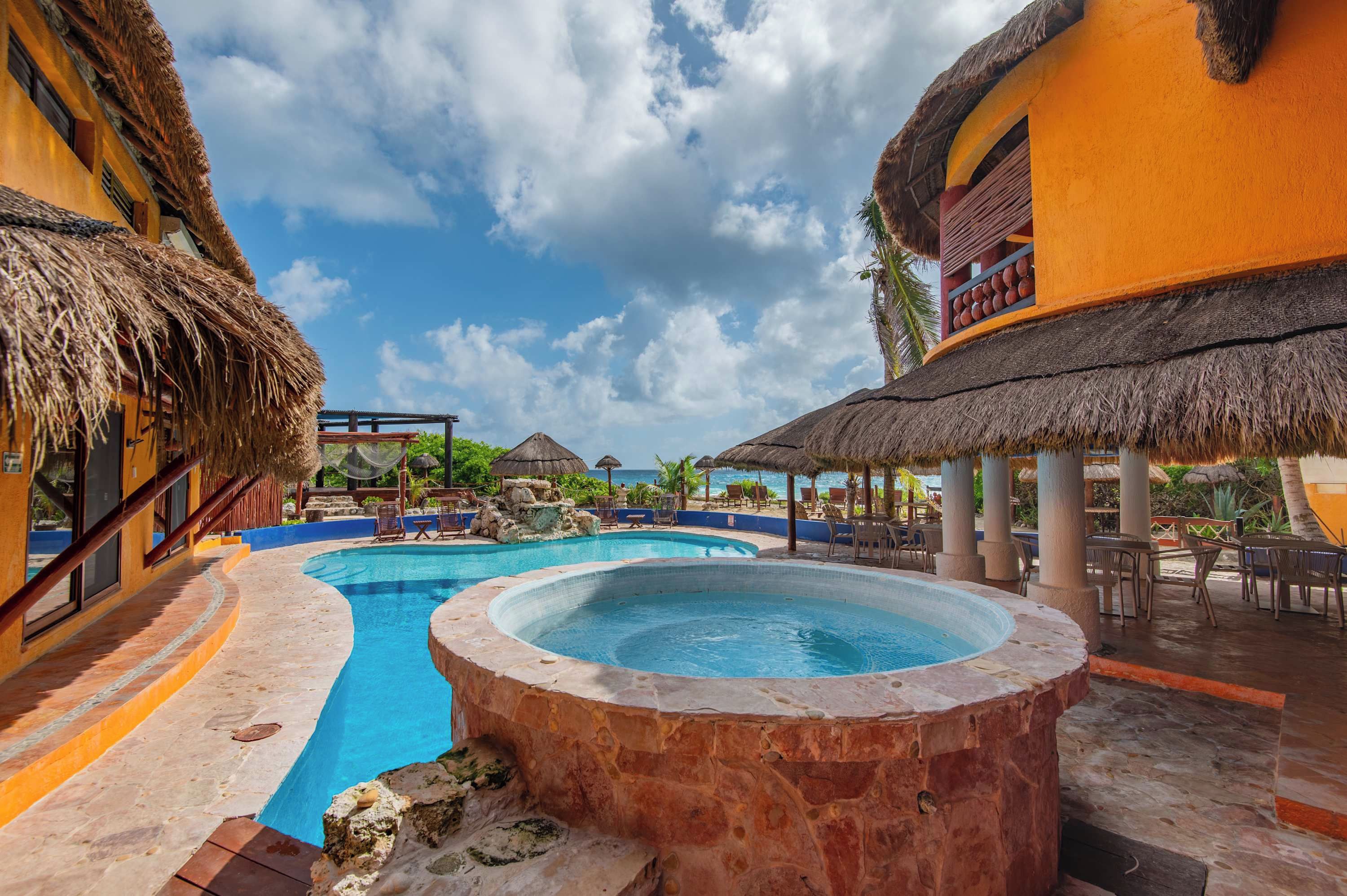 Zona de piscina en un resort con un jacuzzi, estructuras de techo de paja y mobiliario de exterior.