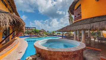 Zona de piscina en un resort con un jacuzzi, estructuras de techo de paja y mobiliario de exterior.
