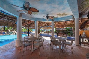 An outdoor pool area with thatched roofs, lounge chairs, and tables. - Bella Mar: Ocean Front w/ Pool Views (Isla Mujeres)
