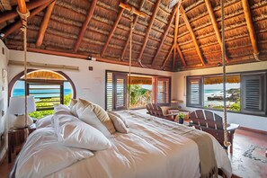 A bedroom with a bed, a chair, a table, and a view of the ocean. - Bella Mar: Ocean Front w/ Pool Views (Isla Mujeres)