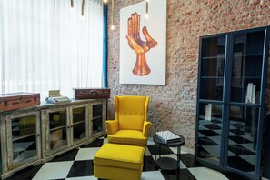 A room with a brick wall, a yellow armchair, a small table, and a cabinet with glass doors. - Studio Bilbao: Roma Norte Rooftop (Ciudad de México)