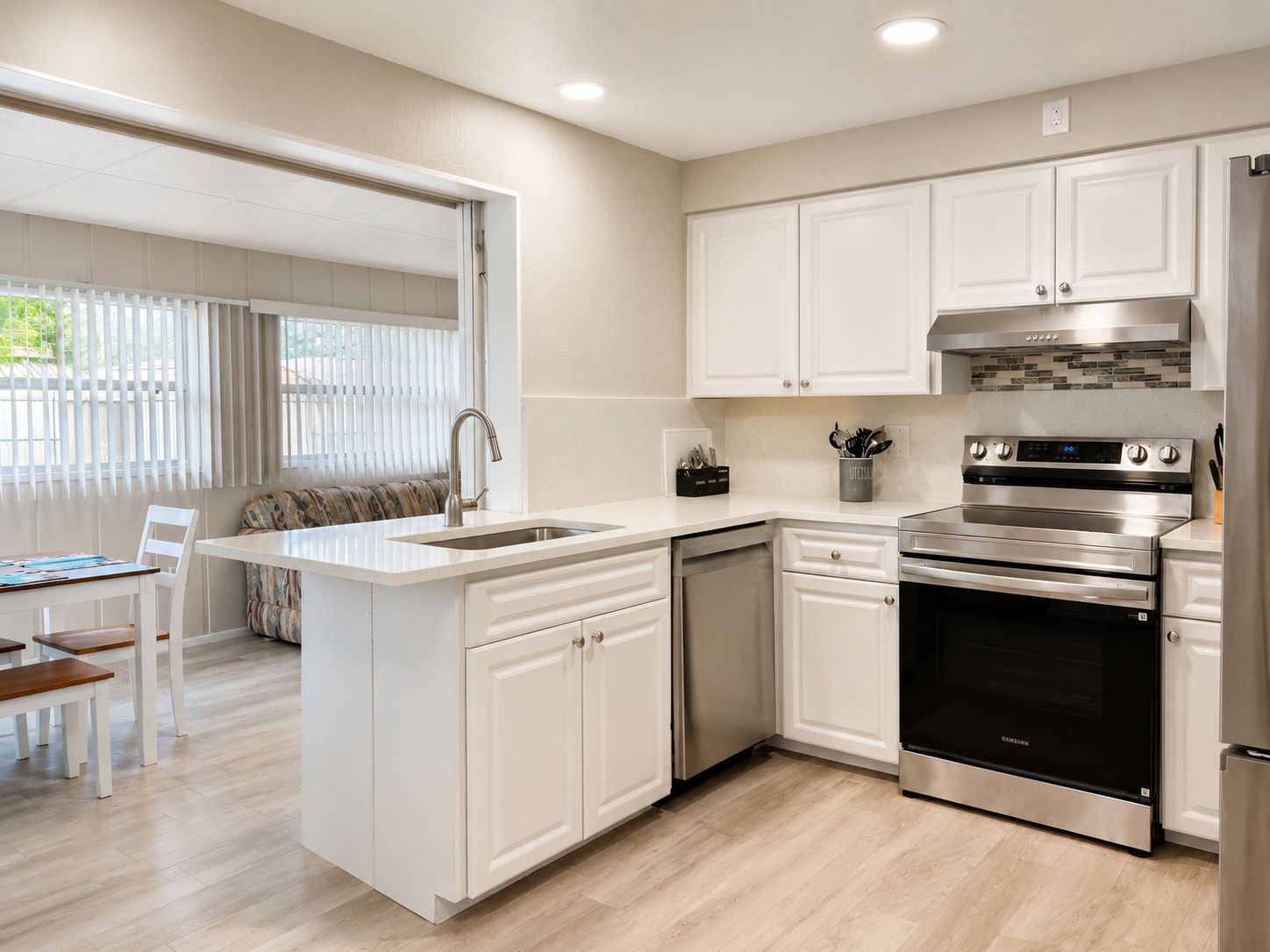 A modern kitchen with white cabinetry, stainless steel appliances, and a dining area with a bench and table.