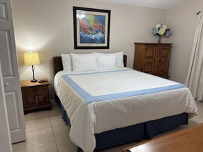 A hotel room with a bed, a nightstand with a lamp, a wooden dresser, and a framed painting on the wall. - Welcome to Maysons Cozy Nest, a comfortable 3 bedroom home in Kissimmee, Fl. (Kissimmee)