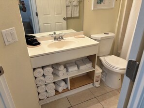 Ein Badezimmer mit einem weißen Waschbecken, einer Toilette und einem Regal mit ordentlich aufgerollten Handtüchern.