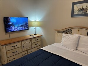 Ein Hotelzimmer mit einem Bett, einem an der Wand befestigten Fernseher, einem Holzschrank und einer Lampe.