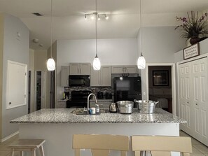 A kitchen with granite countertops, a black refrigerator, a microwave, and a stove. There are three pendant lights hanging from the ceiling. - Welcome to Maysons Cozy Nest, a comfortable 3 bedroom home in Kissimmee, Fl. (Kissimmee)