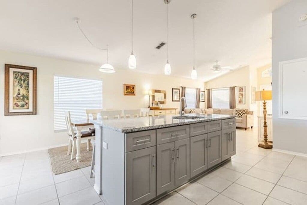 A modern kitchen with a central island, pendant lighting, and a dining area with chairs.