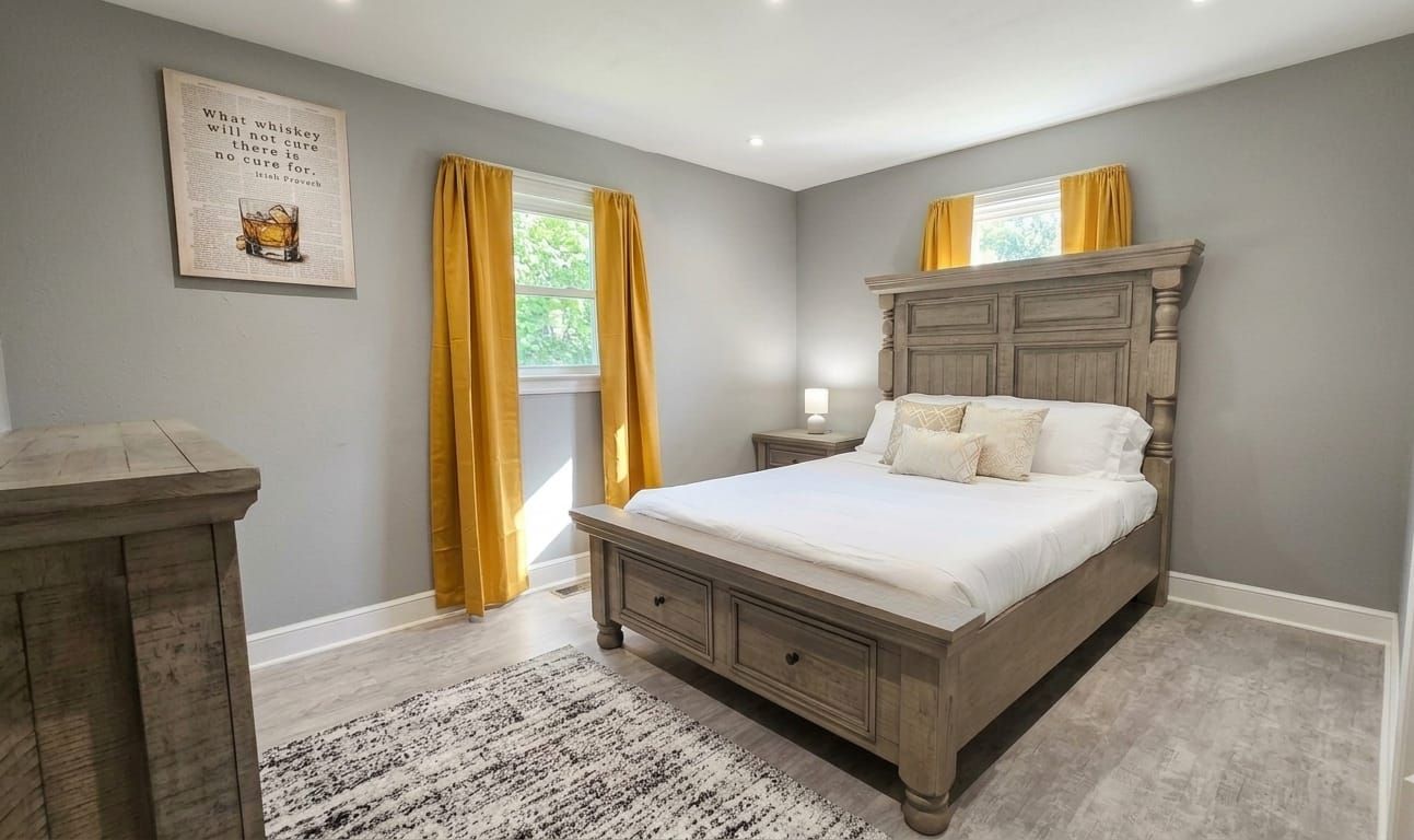 A bedroom with a wooden bed, a nightstand, a lamp, and a window with curtains.