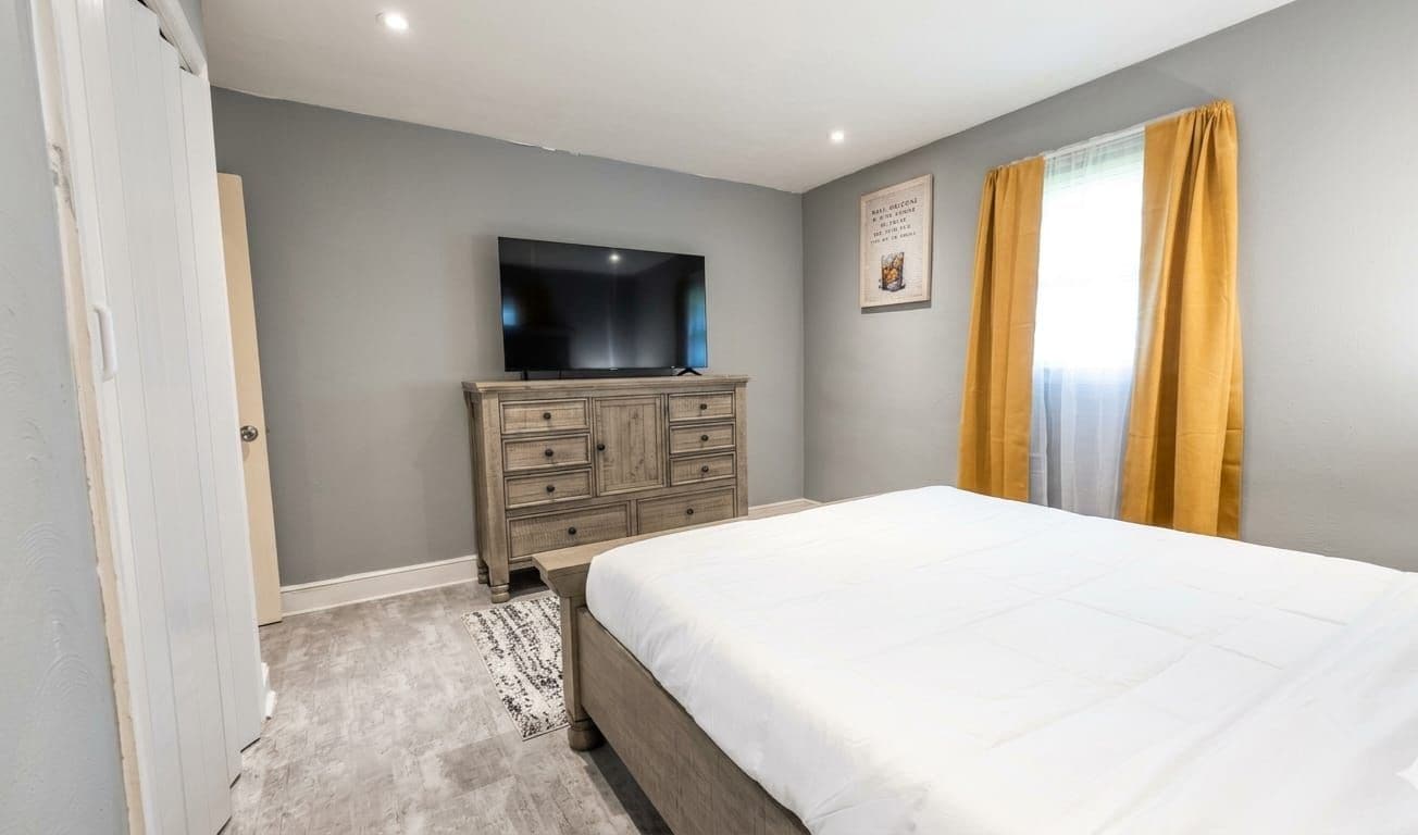 Ein Schlafzimmer mit einem Bett, einem Schminktisch, einem Fernseher und einem Fenster mit Vorhängen.