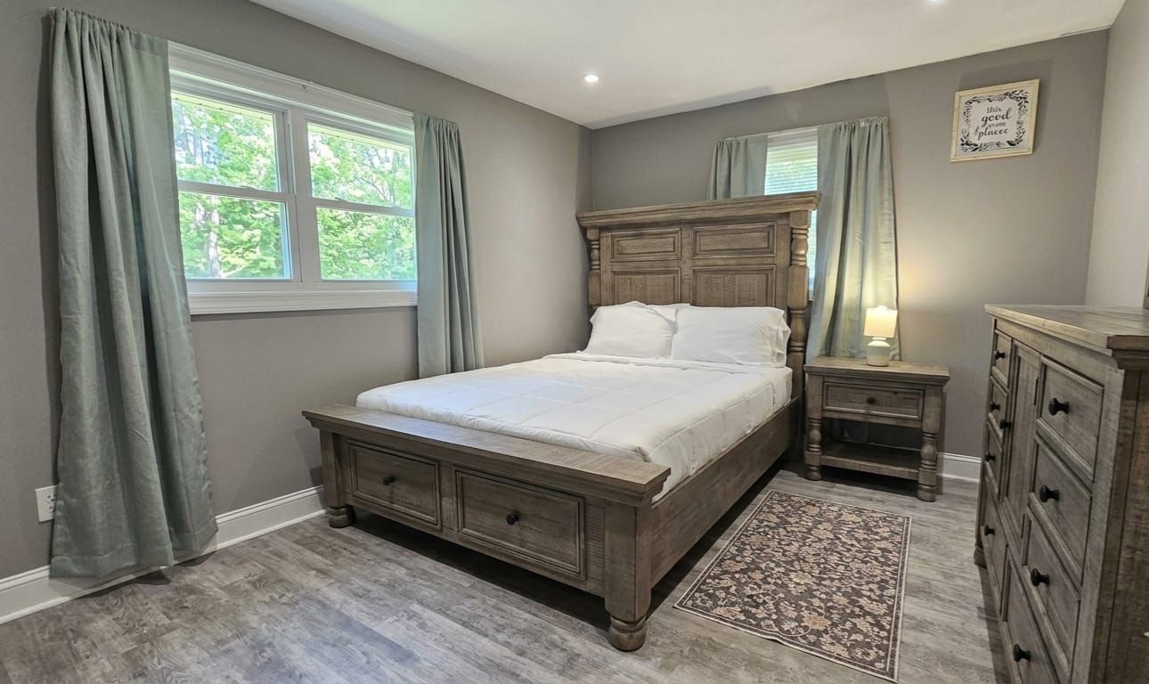Une chambre à coucher avec un lit, des tables de chevet, une commode et une fenêtre avec des rideaux.