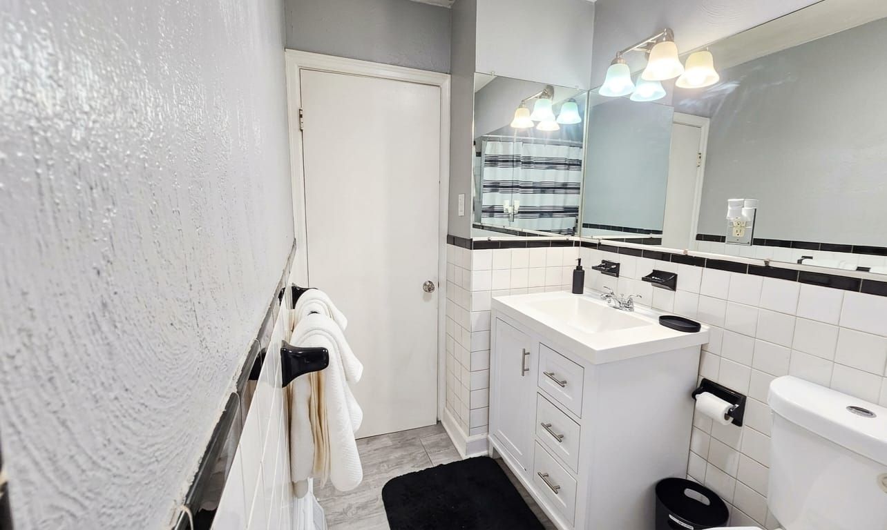 Un baño con un lavamanos blanco, espejo y paredes con azulejos negros.