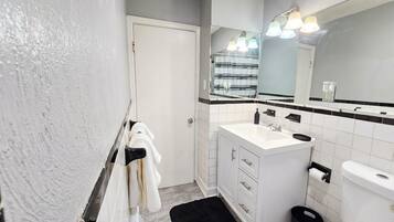 Un baño con un lavamanos blanco, espejo y paredes con azulejos negros.