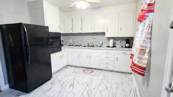 Cozinha com armários brancos, geladeira preta e piso de mármore.