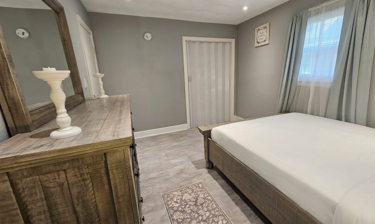 Ein Schlafzimmer mit Bett, Kommode, Spiegel und einer Tür.