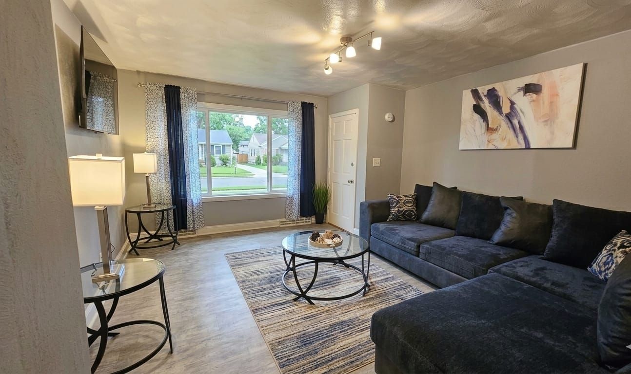 A living room with a sofa, a coffee table, a lamp, and a view of the outside.